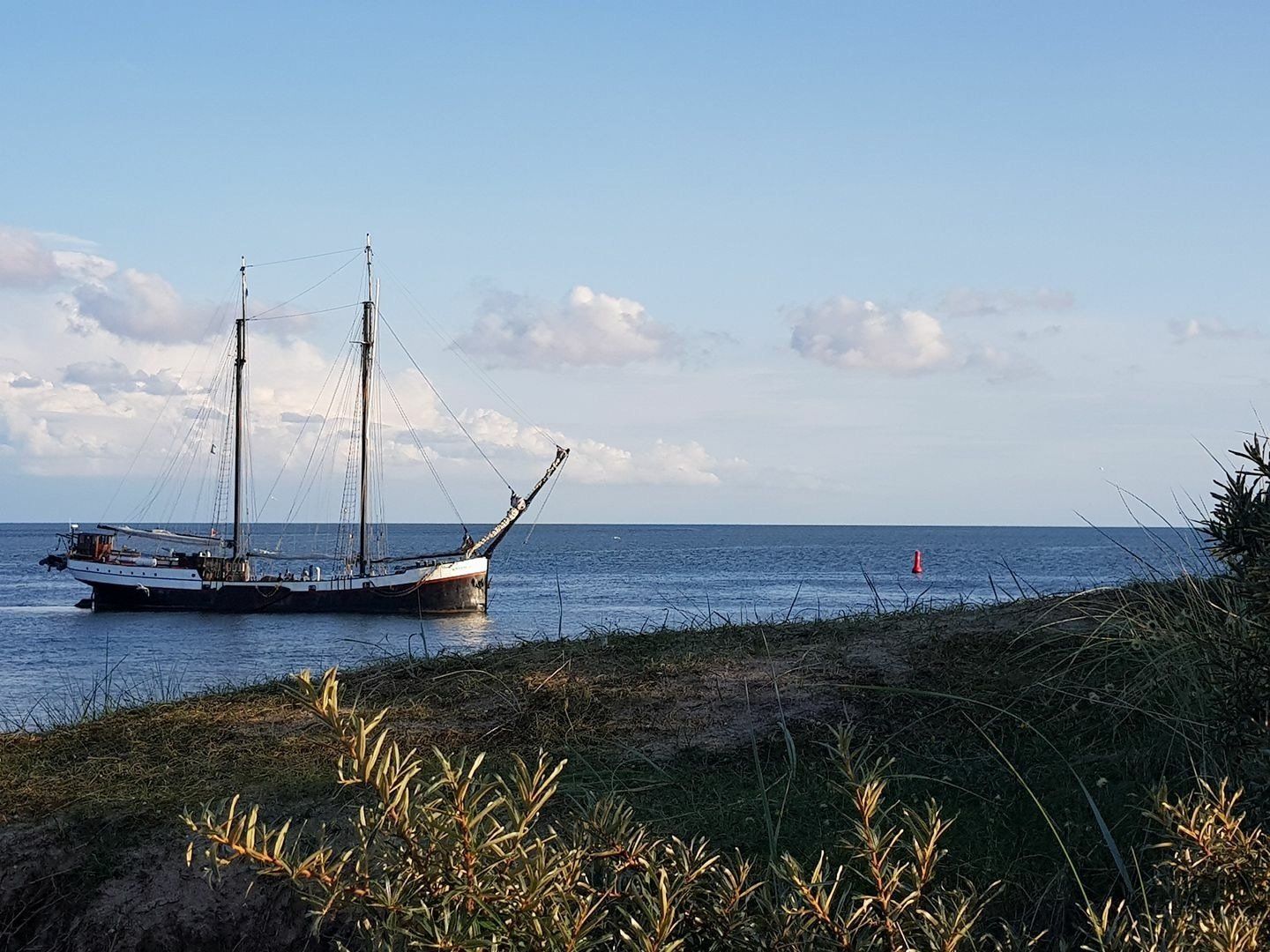 Segelschiff auf dem Meer in der Nähe des grasbewachsenen Ufers unter einem teilweise bewölkten blauen Himmel.