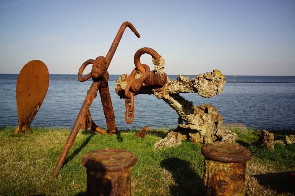Rostige Anker auf einer Rasenfläche am Meer unter blauem Himmel. Auf dem Watteninsel Terschelling