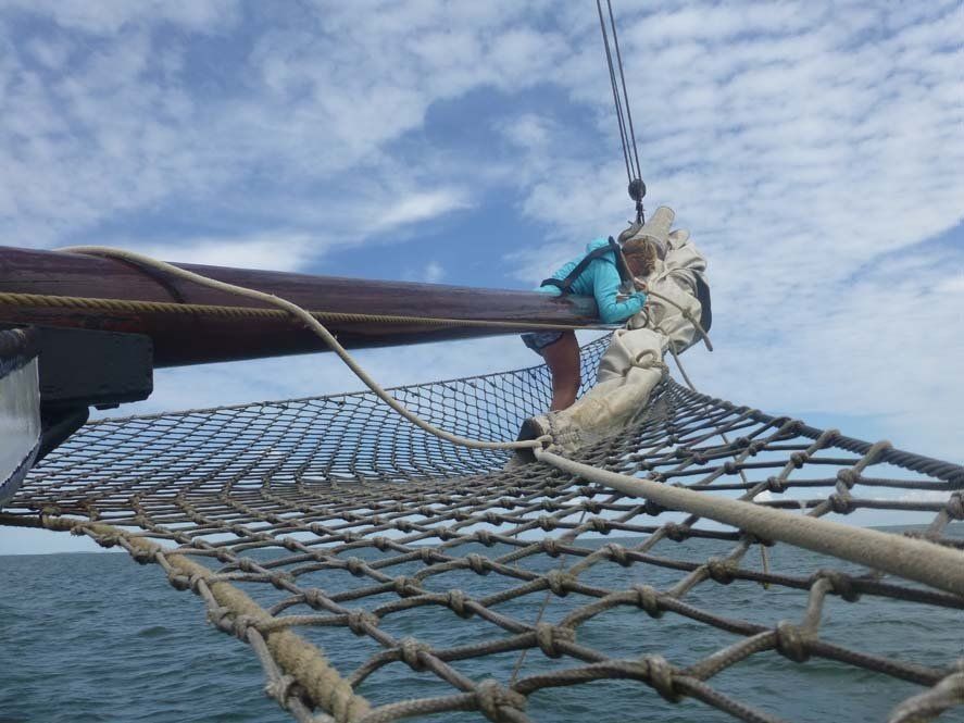 Segelbootbug mit einem Netz und einer Person in Blau vor einem teilweise bewölkten Himmel.