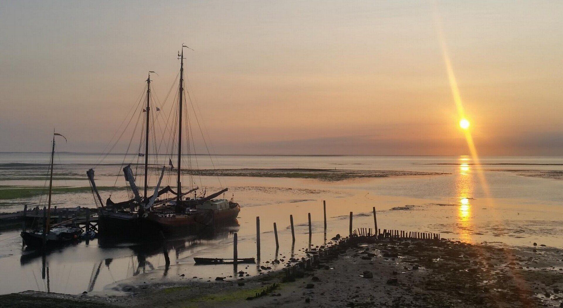 Boote legten bei Sonnenuntergang an. Orangefarbener Himmel spiegelt sich im Wasser. Silhouetten.