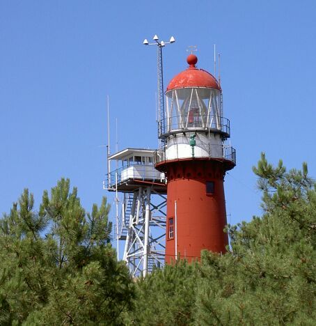 Rot-weißer Leuchtturm von Watteninsel Vlieland mit Aussichtsplattform und Bäumen vor blauem Himmel.