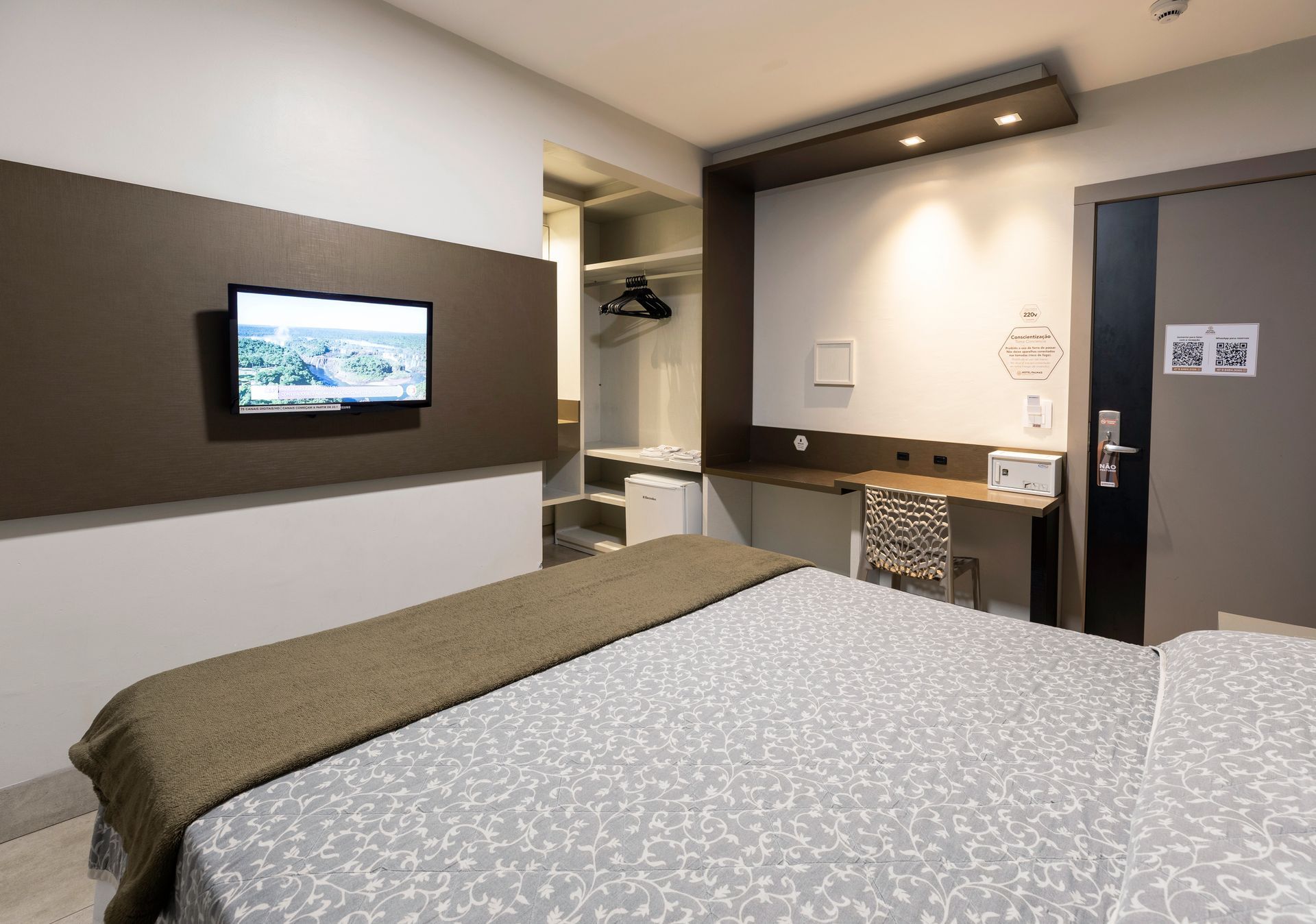 Quarto de hotel moderno com cama, TV de parede e escrivaninha compacta.