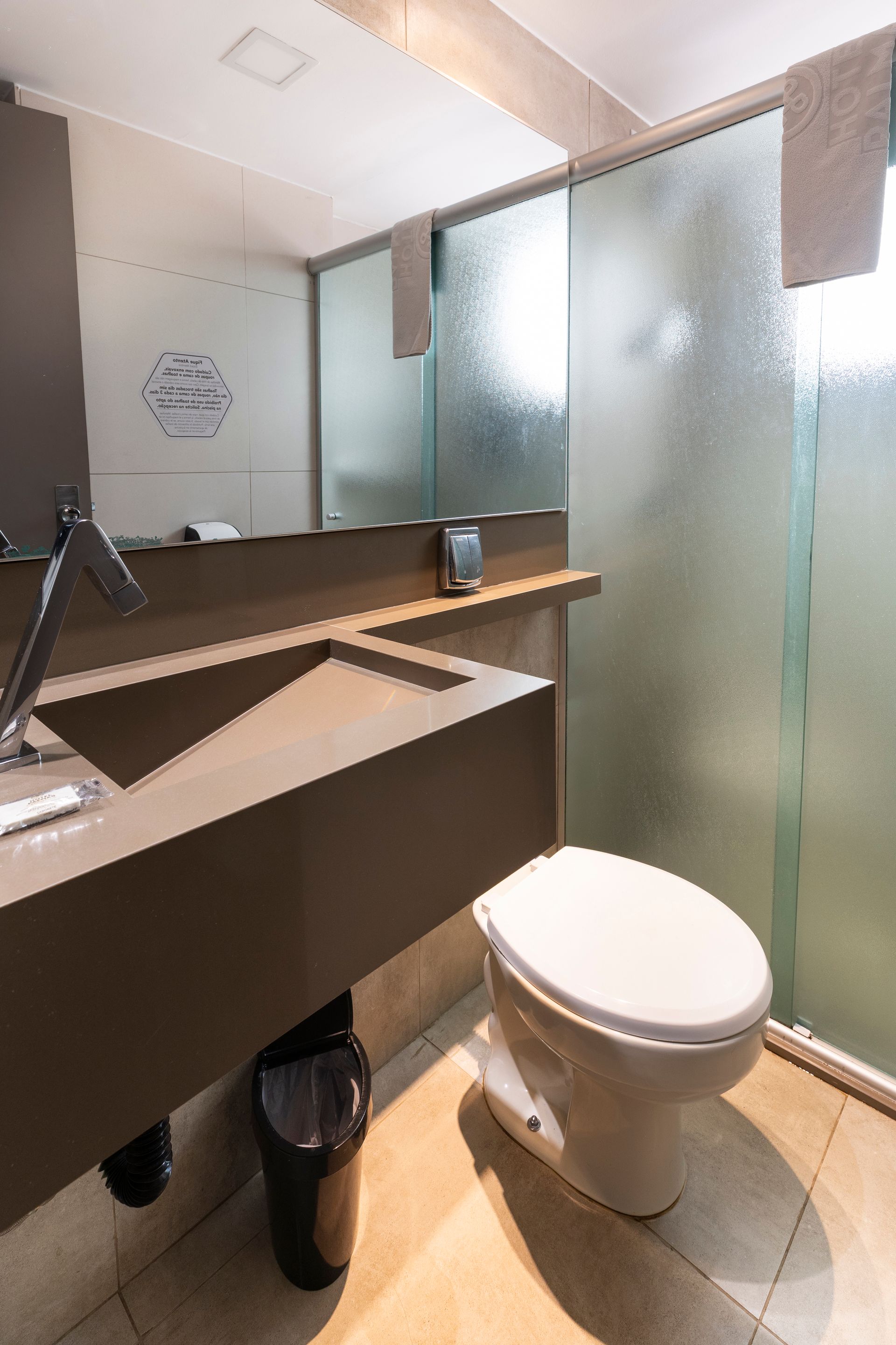 Banheiro moderno com box de vidro fosco, vaso sanitário branco e pia escura.