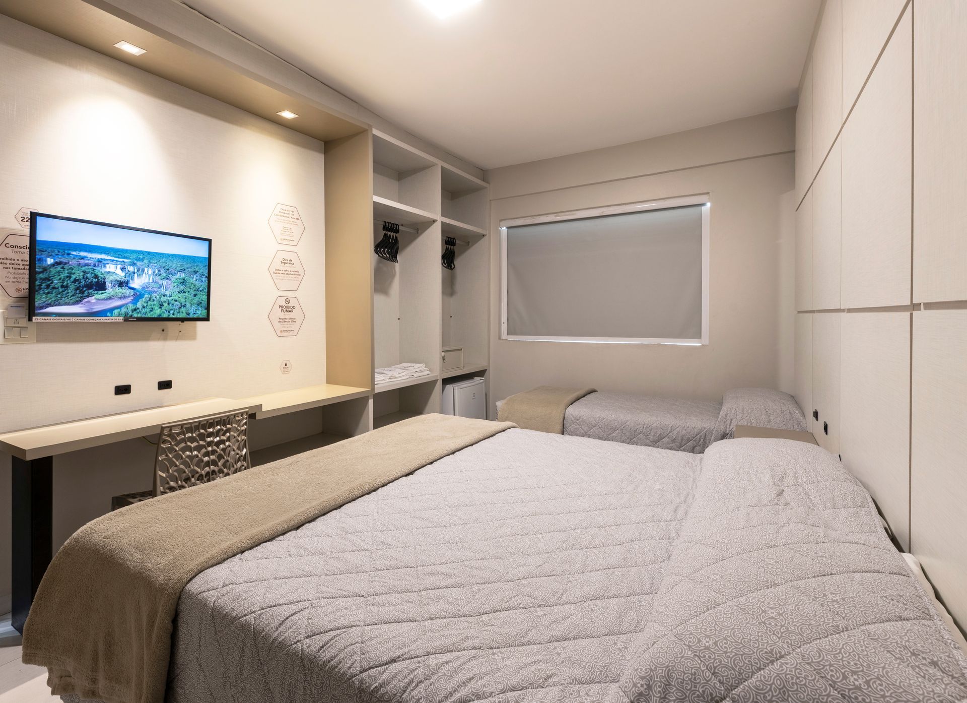 Quarto moderno com cama, TV de parede, armário embutido e janela com persianas.