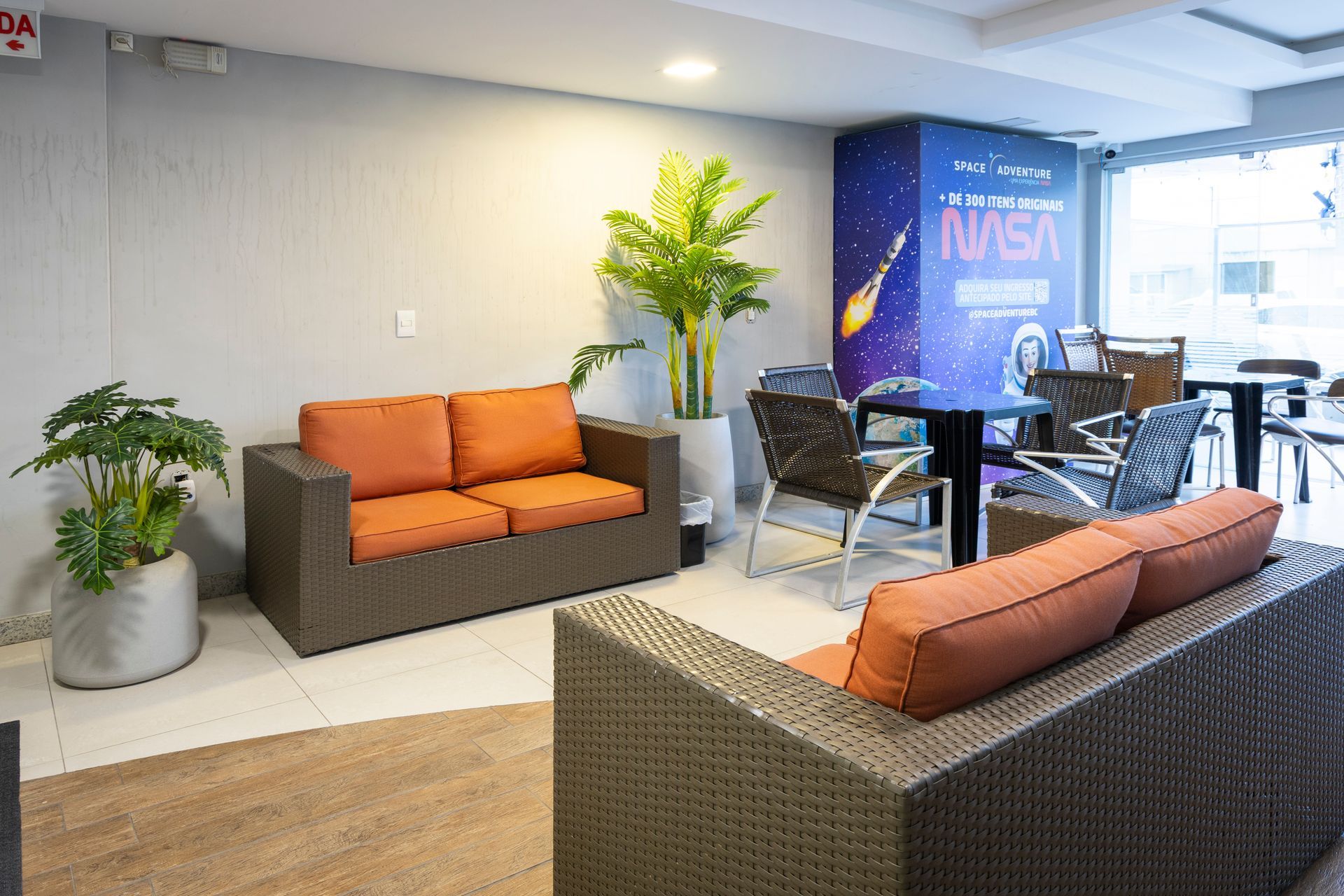 Sala de estar moderna com sofás laranja e cinza, plantas e uma área de exposição com a marca da NASA.