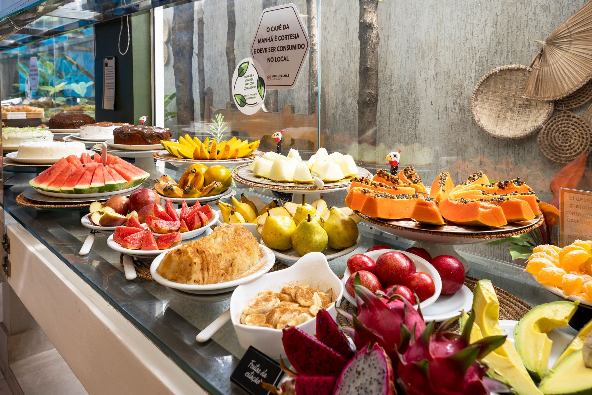 Mesa de bufê com frutas coloridas, doces e sobremesas dispostas em bandejas e travessas.