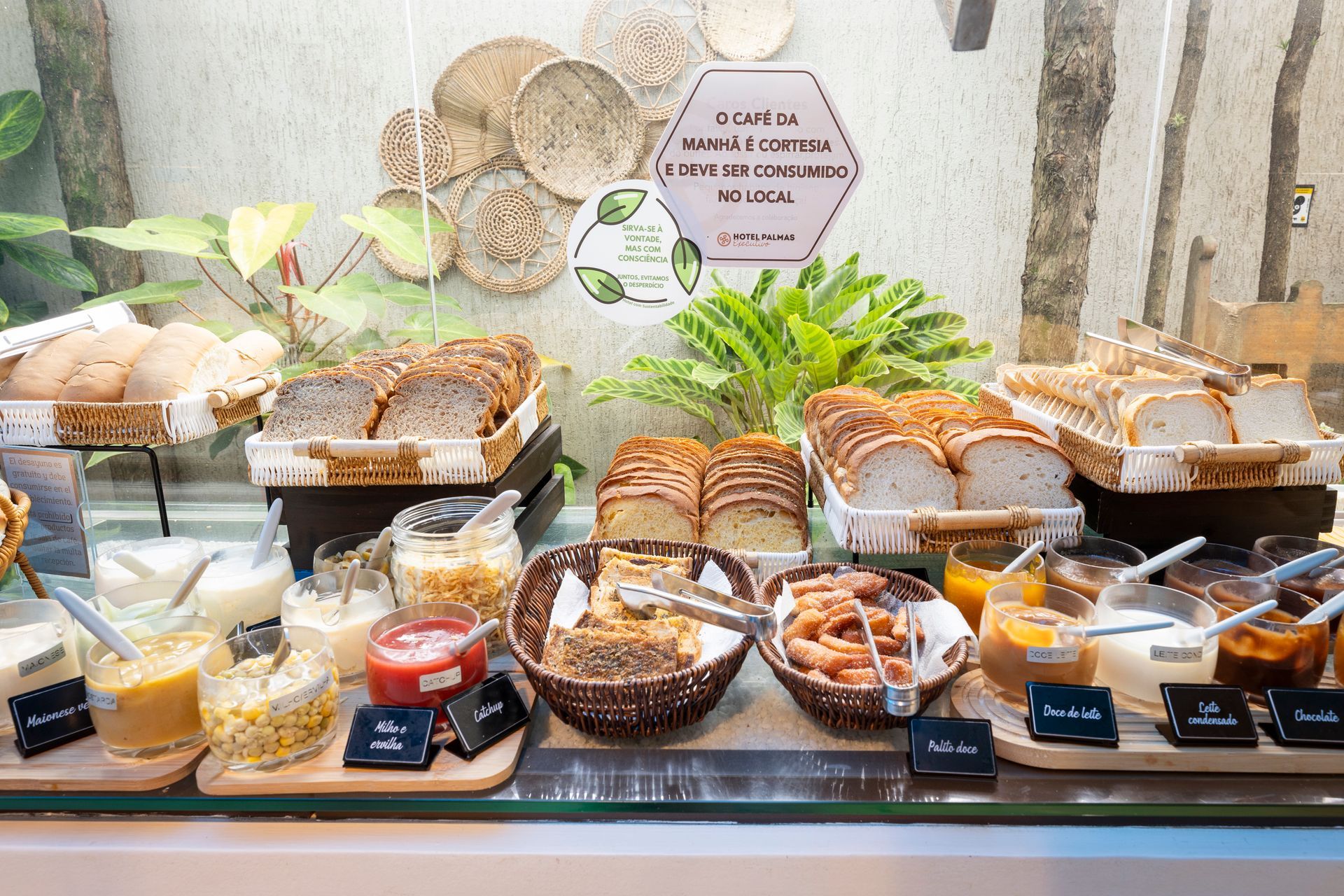 Vitrine de padaria com uma variedade de pães, doces e sobremesas em bandejas atrás de um vidro.