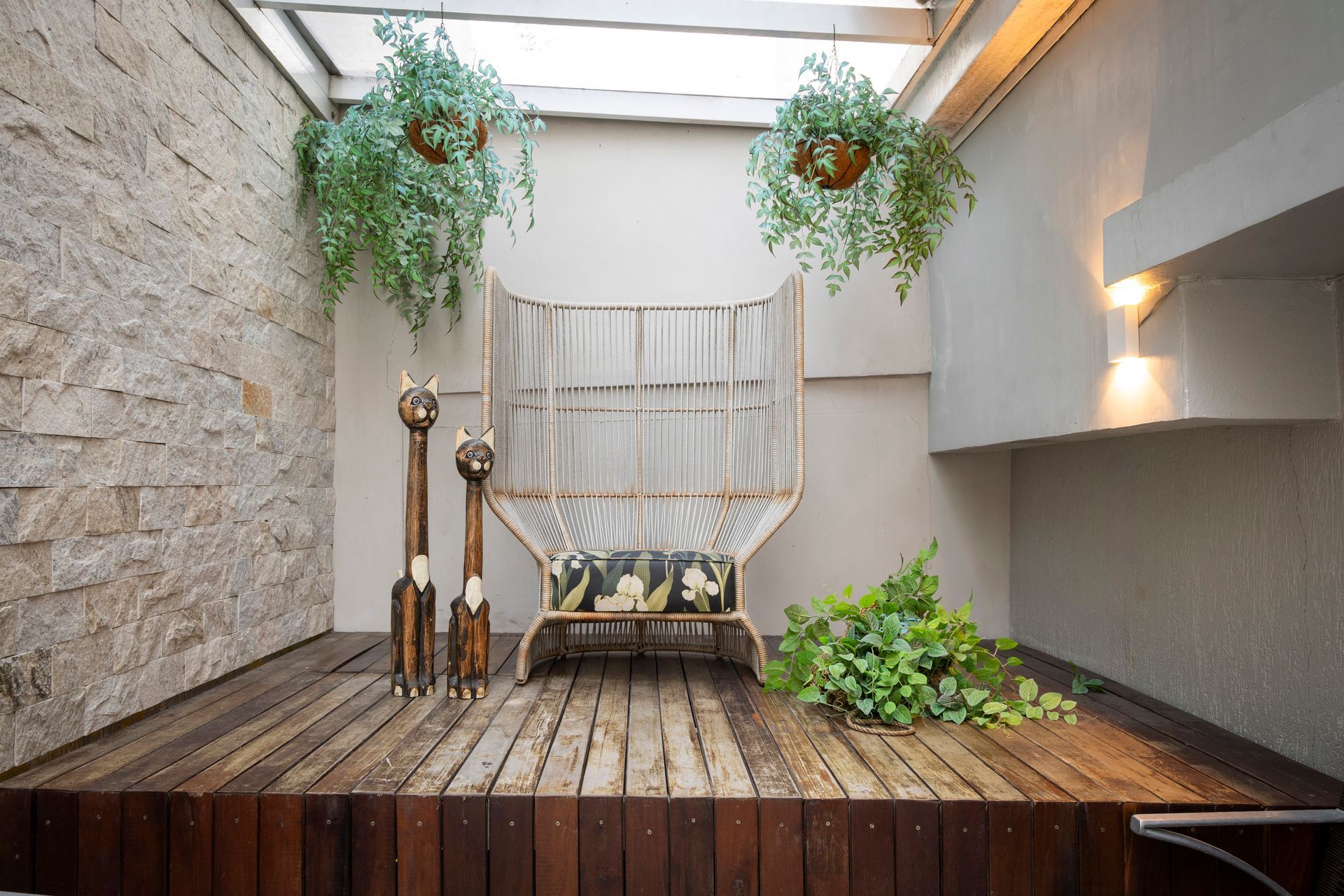 Pátio moderno com deck de madeira, plantas suspensas, cadeira de vime e claraboias em um pátio iluminado.