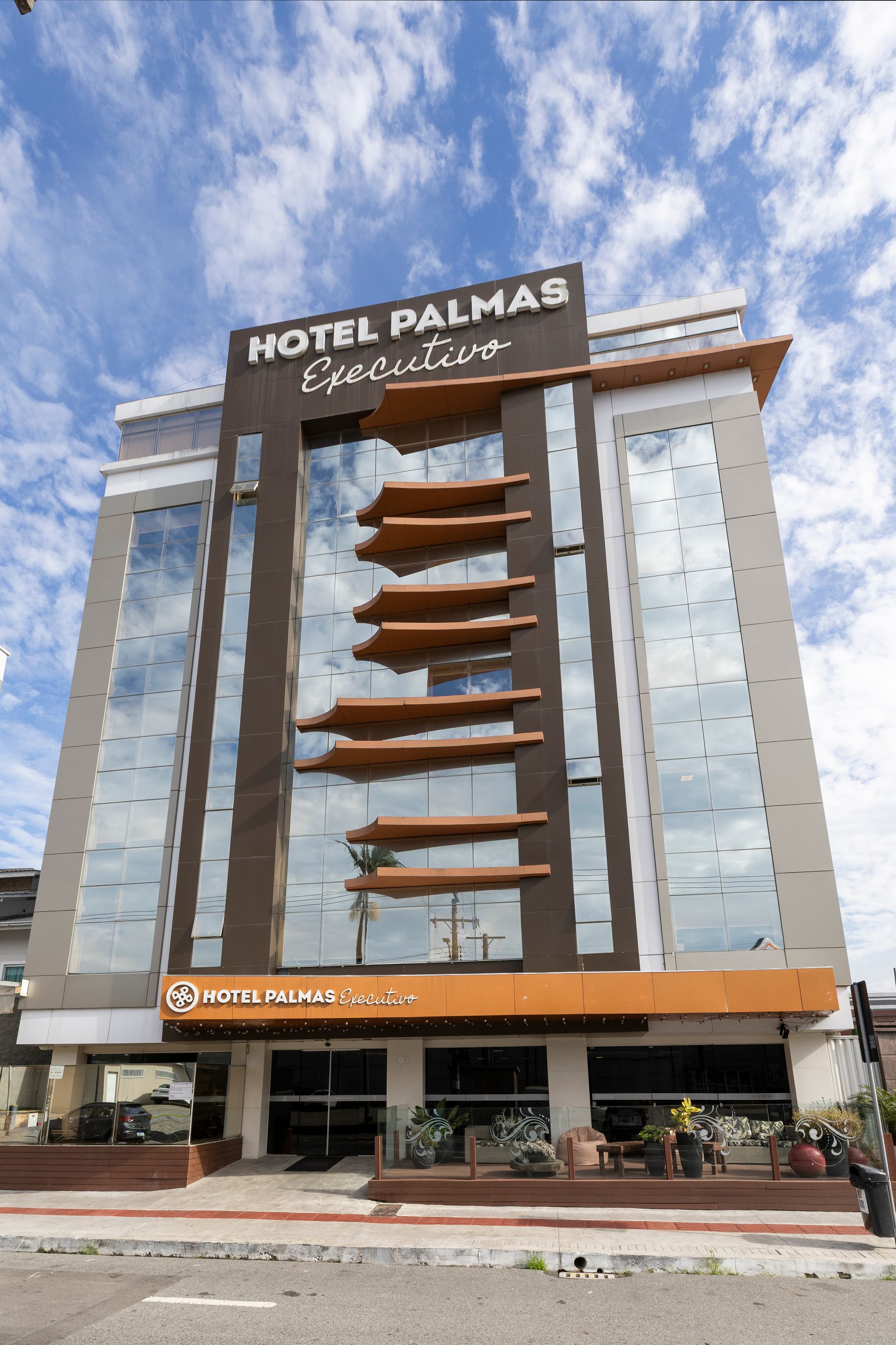 Torre do Hotel Palmas com janelas espelhadas, varandas laranja e um céu nublado ao fundo.