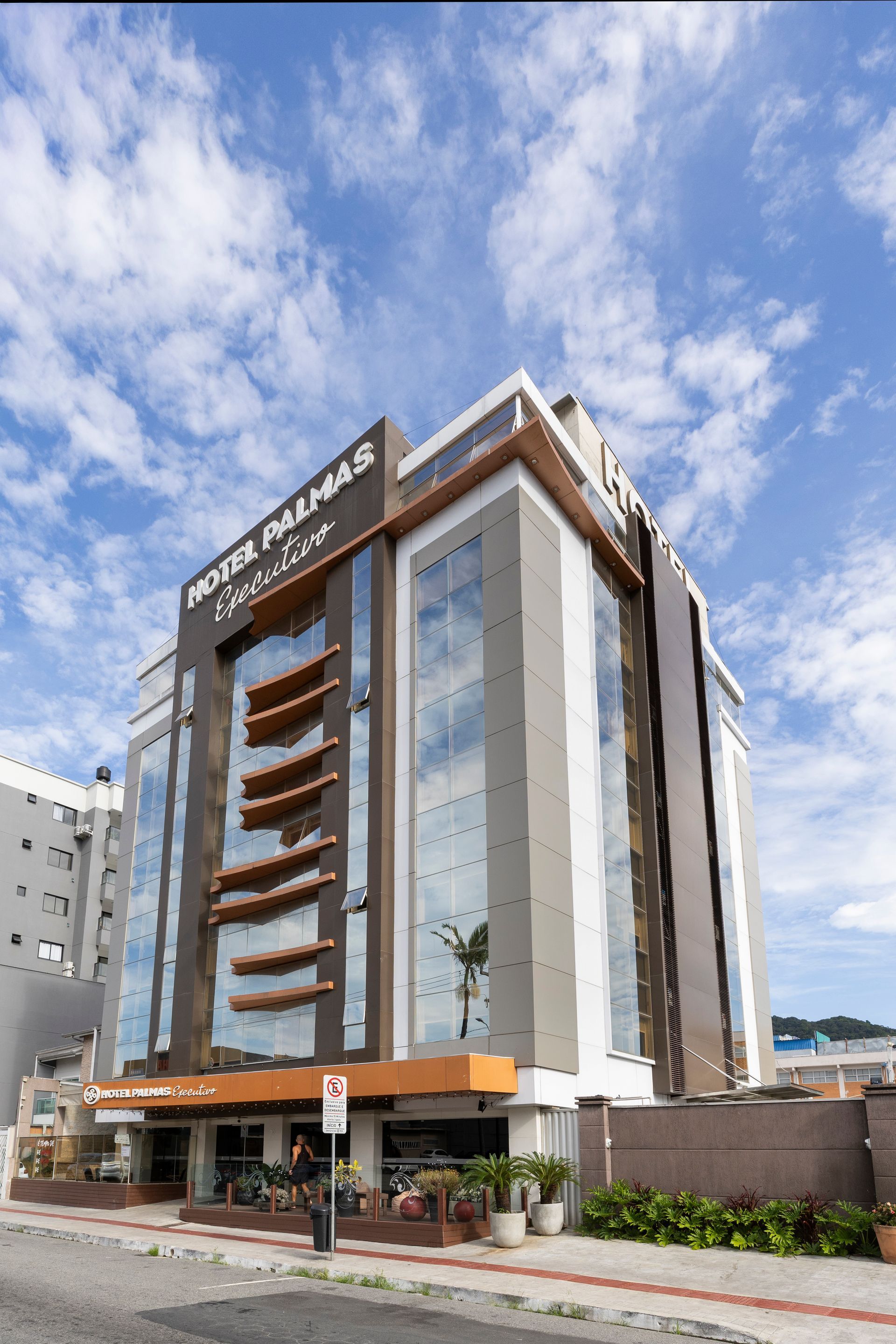 Prédio de escritórios moderno de vários andares com fachada de vidro e detalhes em marrom sob um céu azul e nublado.