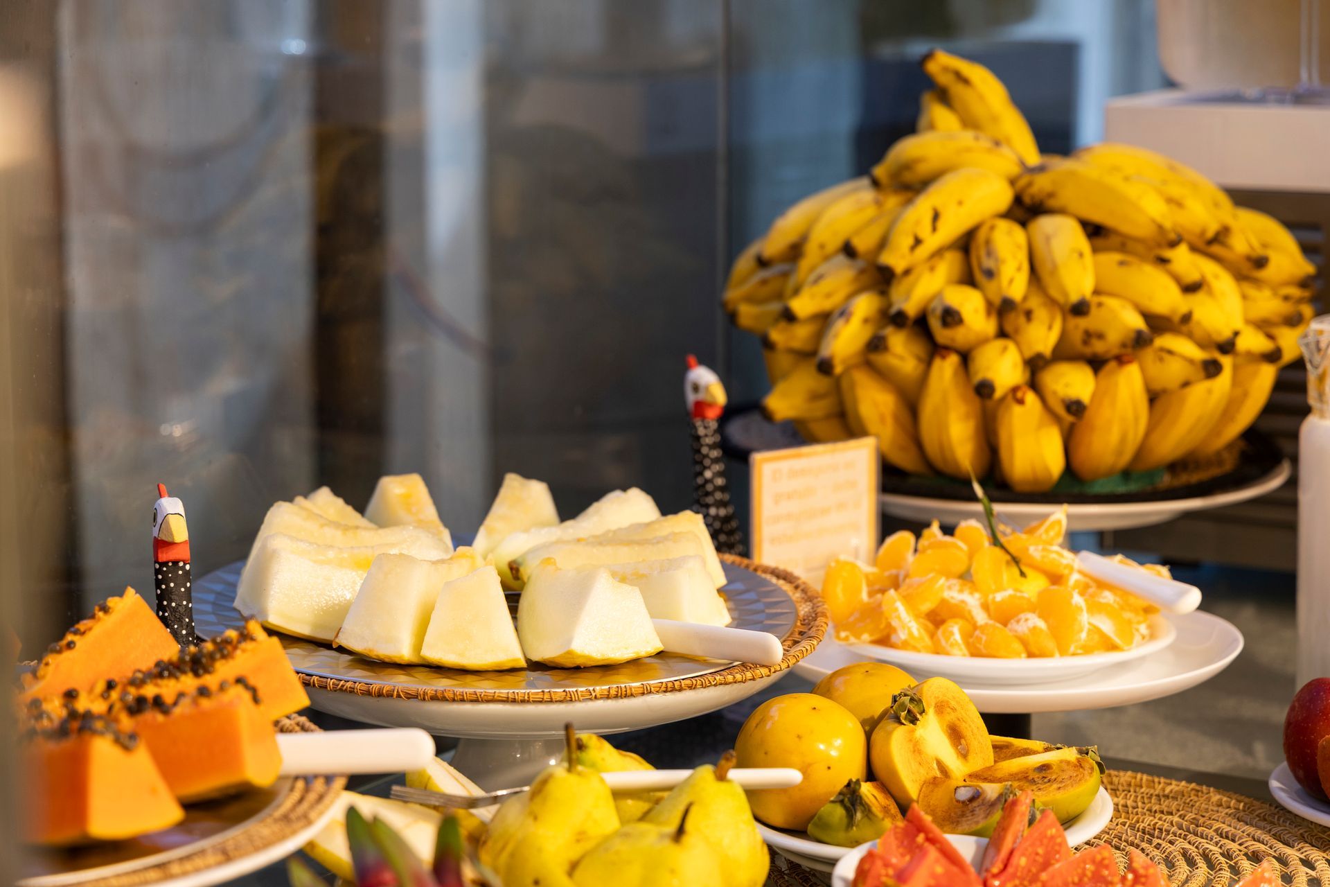 Bananas e frutas variadas dispostas em pratos em uma mesa de bufê.