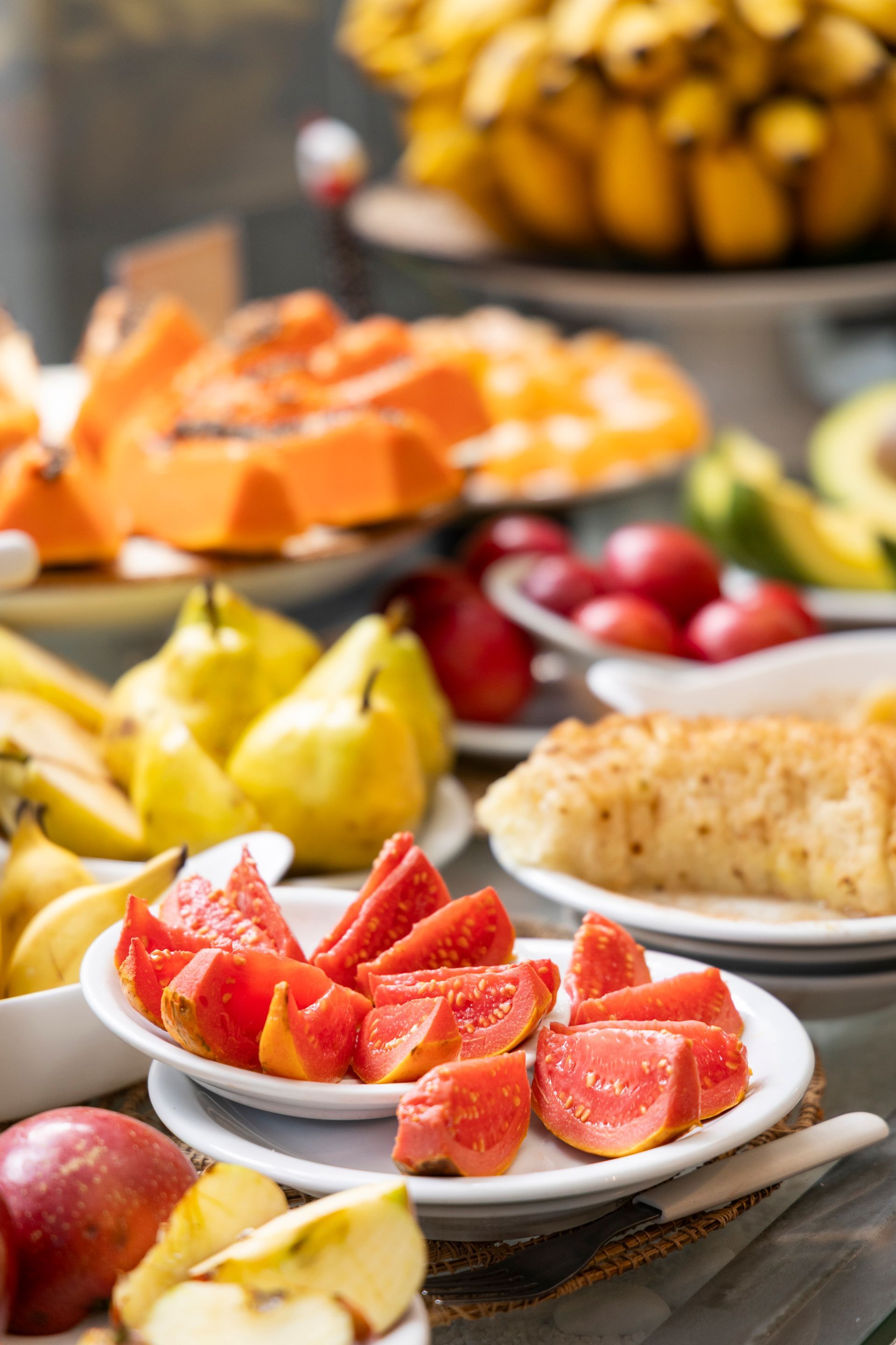 Buffet de frutas com morangos fatiados, bananas e kiwis em pratos brancos.
