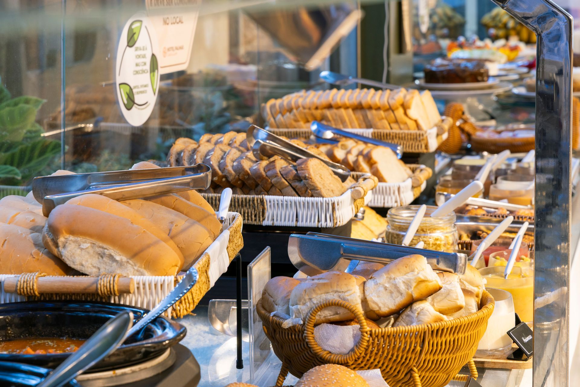 Vitrine de padaria com diversos pães e doces em cestas e bandejas atrás de um vidro.
