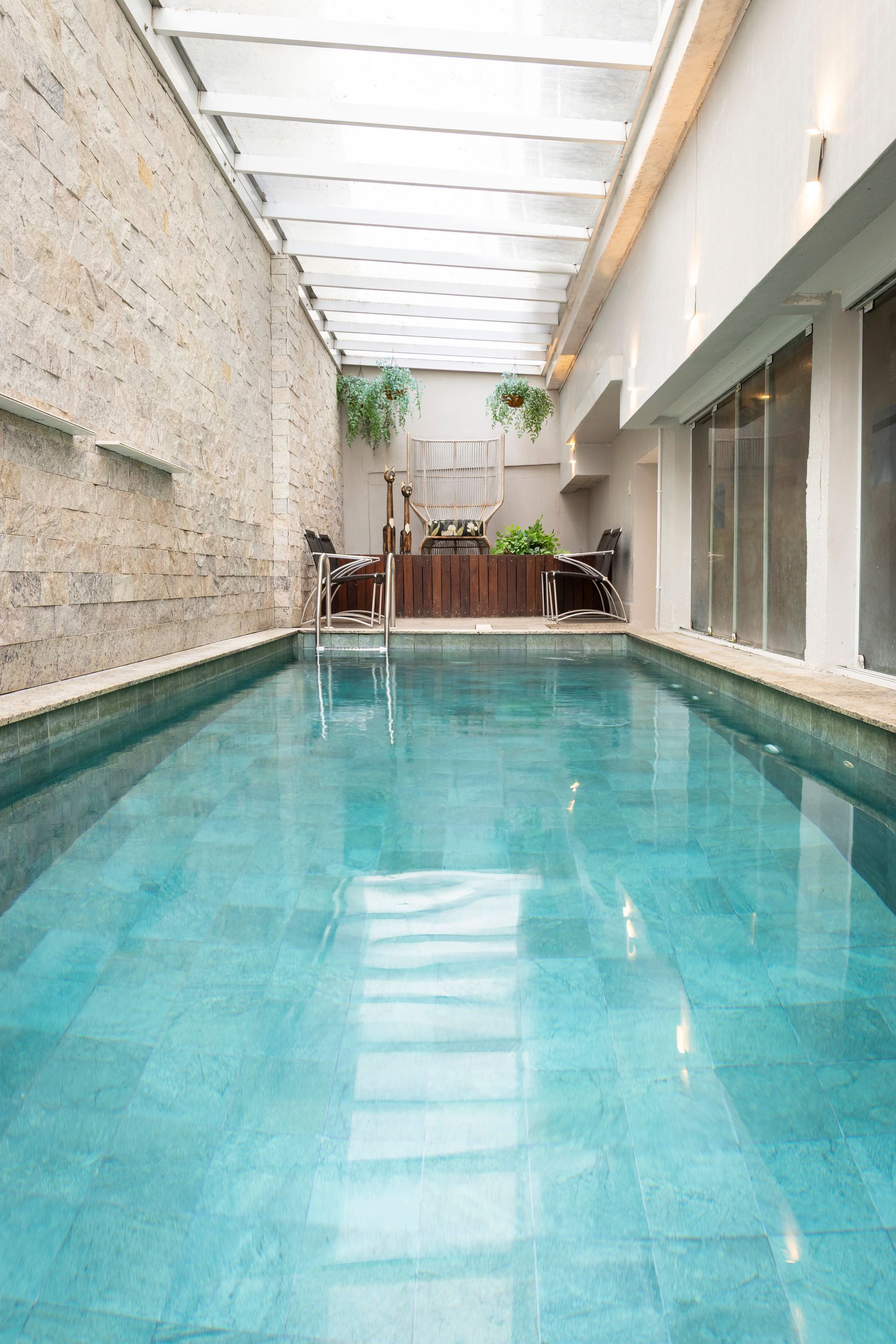 Piscina estreita coberta por uma claraboia, com água turquesa e espreguiçadeiras na extremidade oposta.