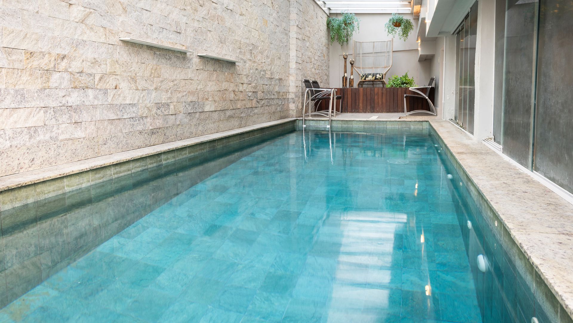 Piscina estreita coberta com água turquesa junto a paredes de pedra e janelas de vidro.