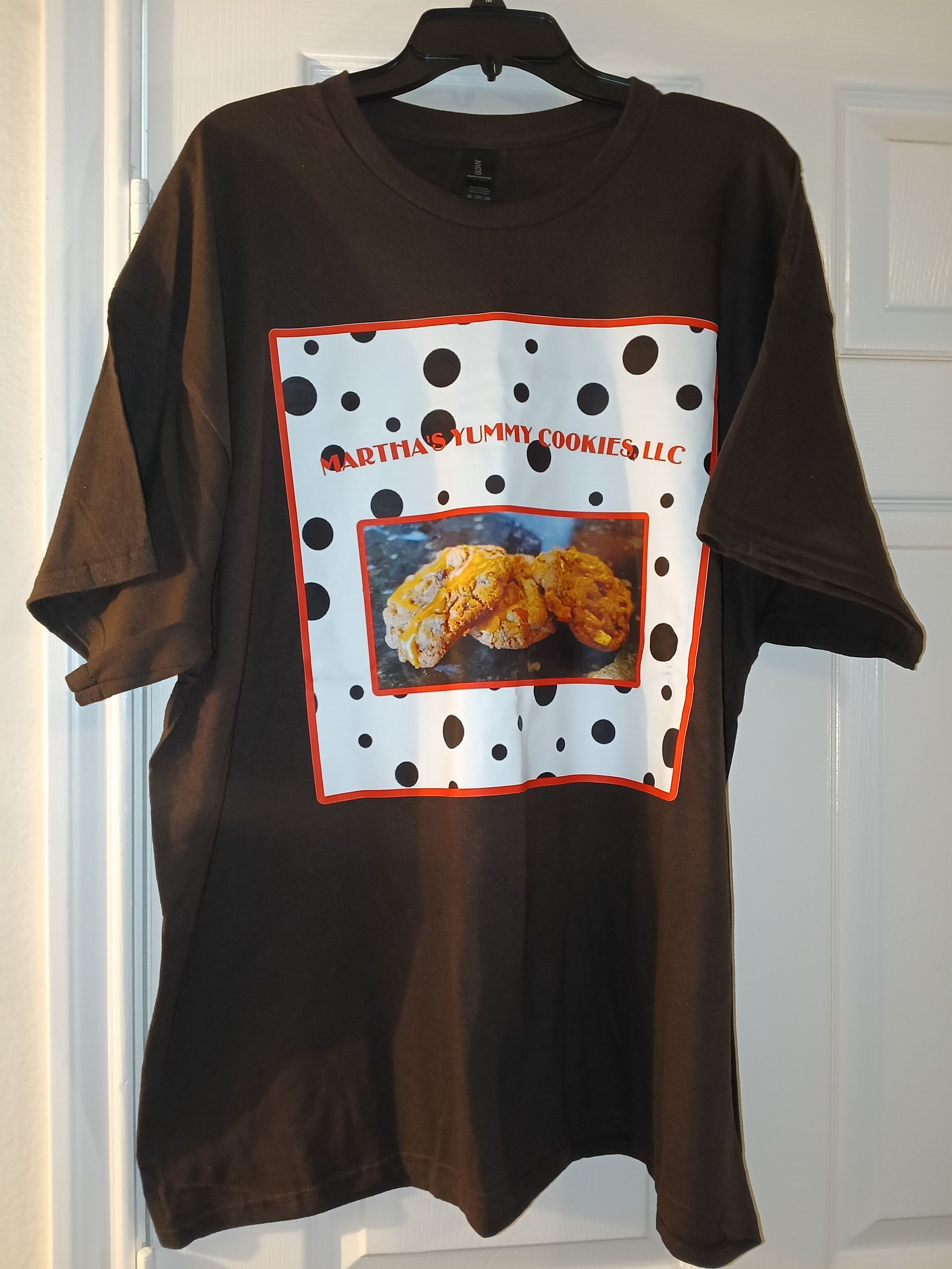 A brown t-shirt featuring a graphic of white fabric with black spots, a red border, and a small photo of fried food.