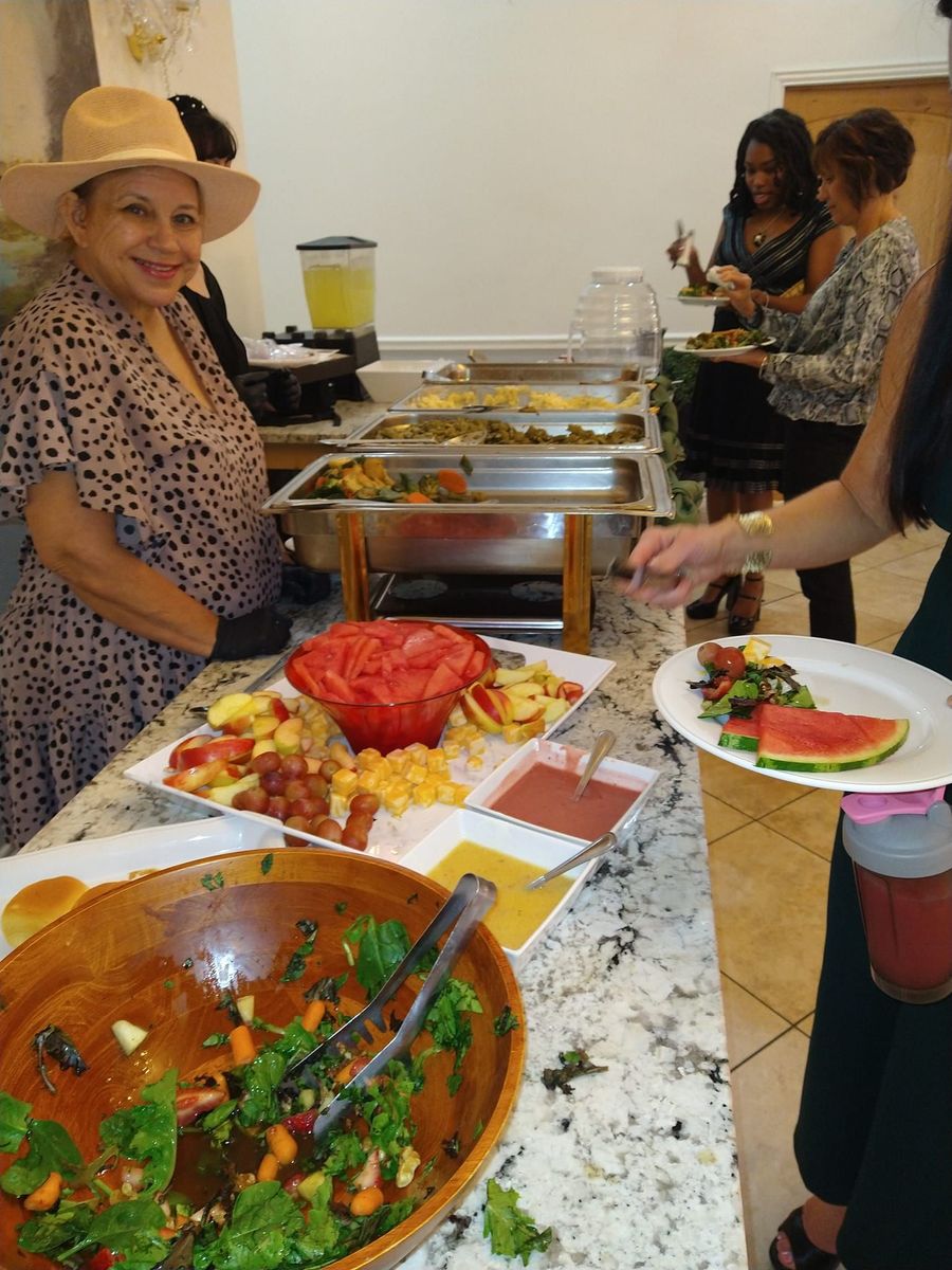 Buffet table with a smiling person in a hat serving food to guests.