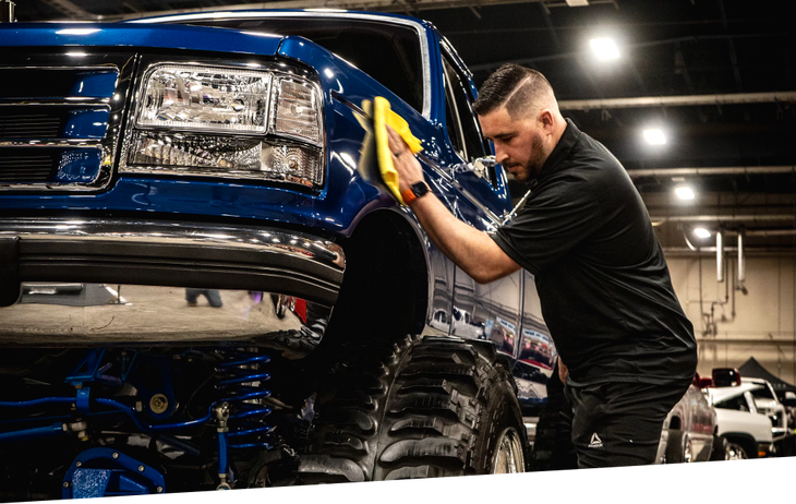 a man is polishing a blue truck with a yellow cloth .