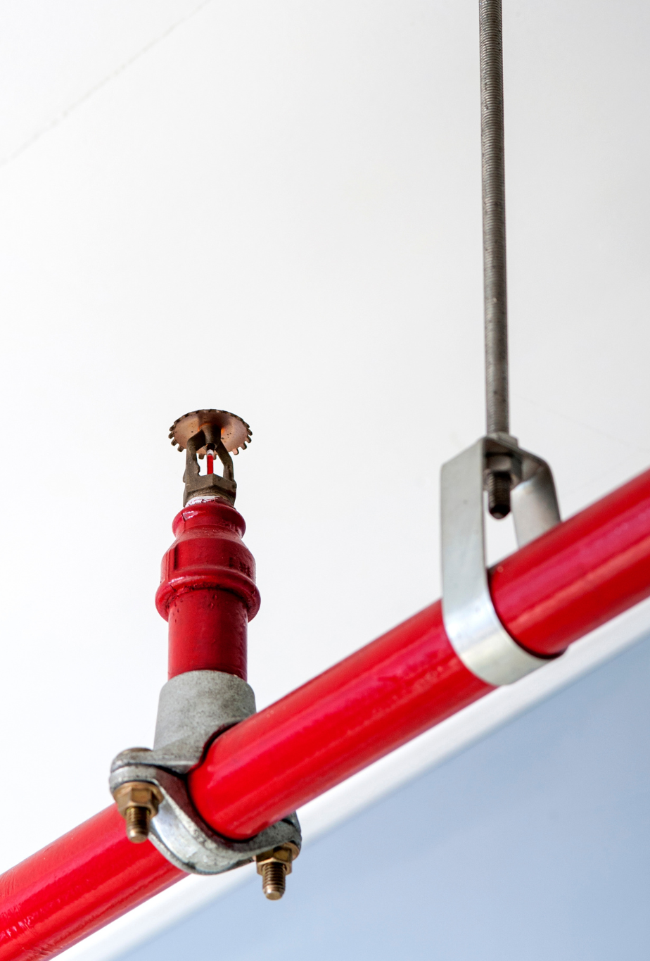 A red pipe with a sprinkler attached to it is hanging from the ceiling.