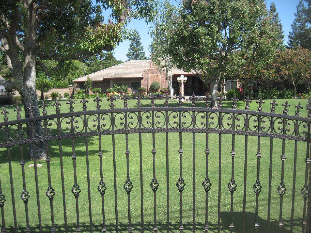 A wrought iron fence surrounds a lush green lawn in front of a house