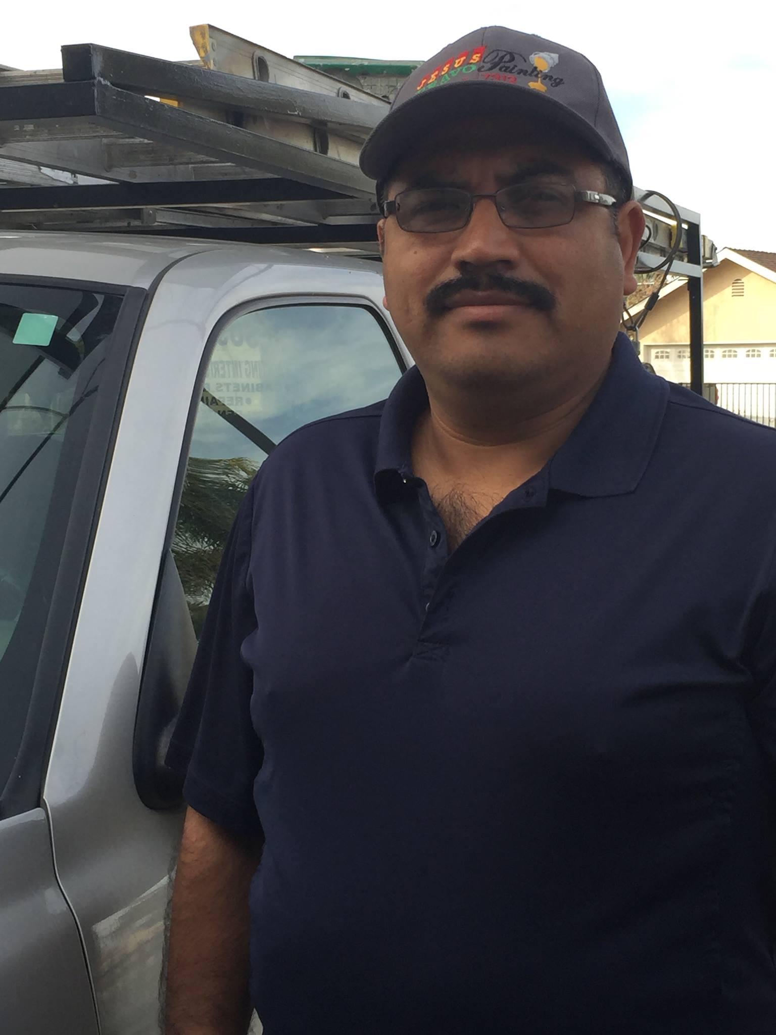 A man with a mustache and glasses is standing in front of a truck.