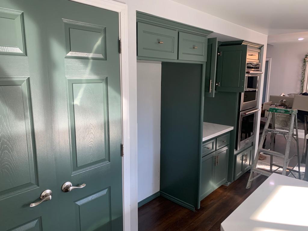 A kitchen with green cabinets and a ladder in the background.