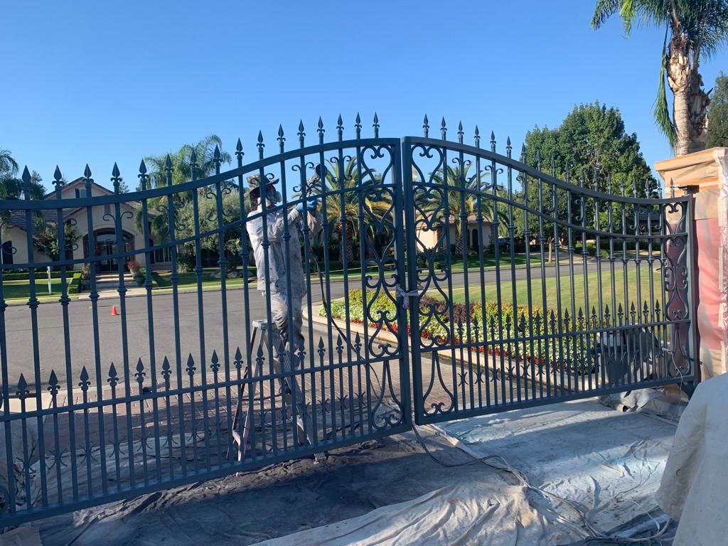A man is painting a wrought iron gate in front of a house.