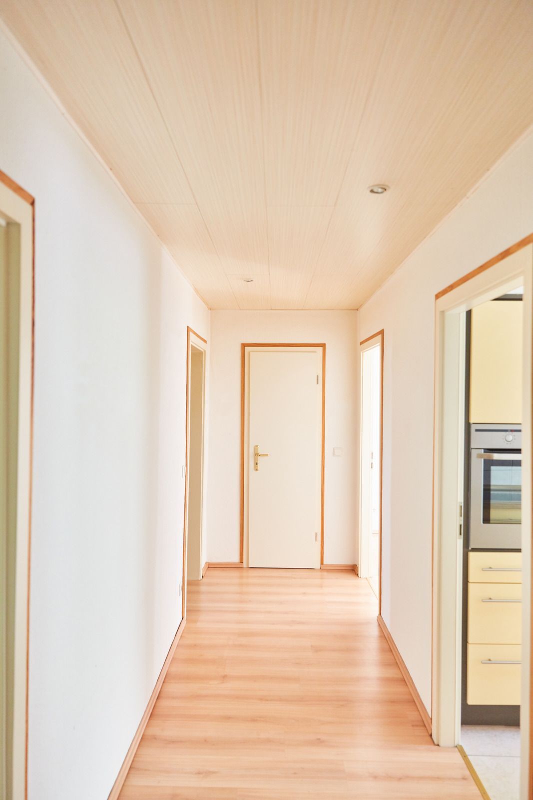 A long hallway with wooden floors and white walls leading to a kitchen.