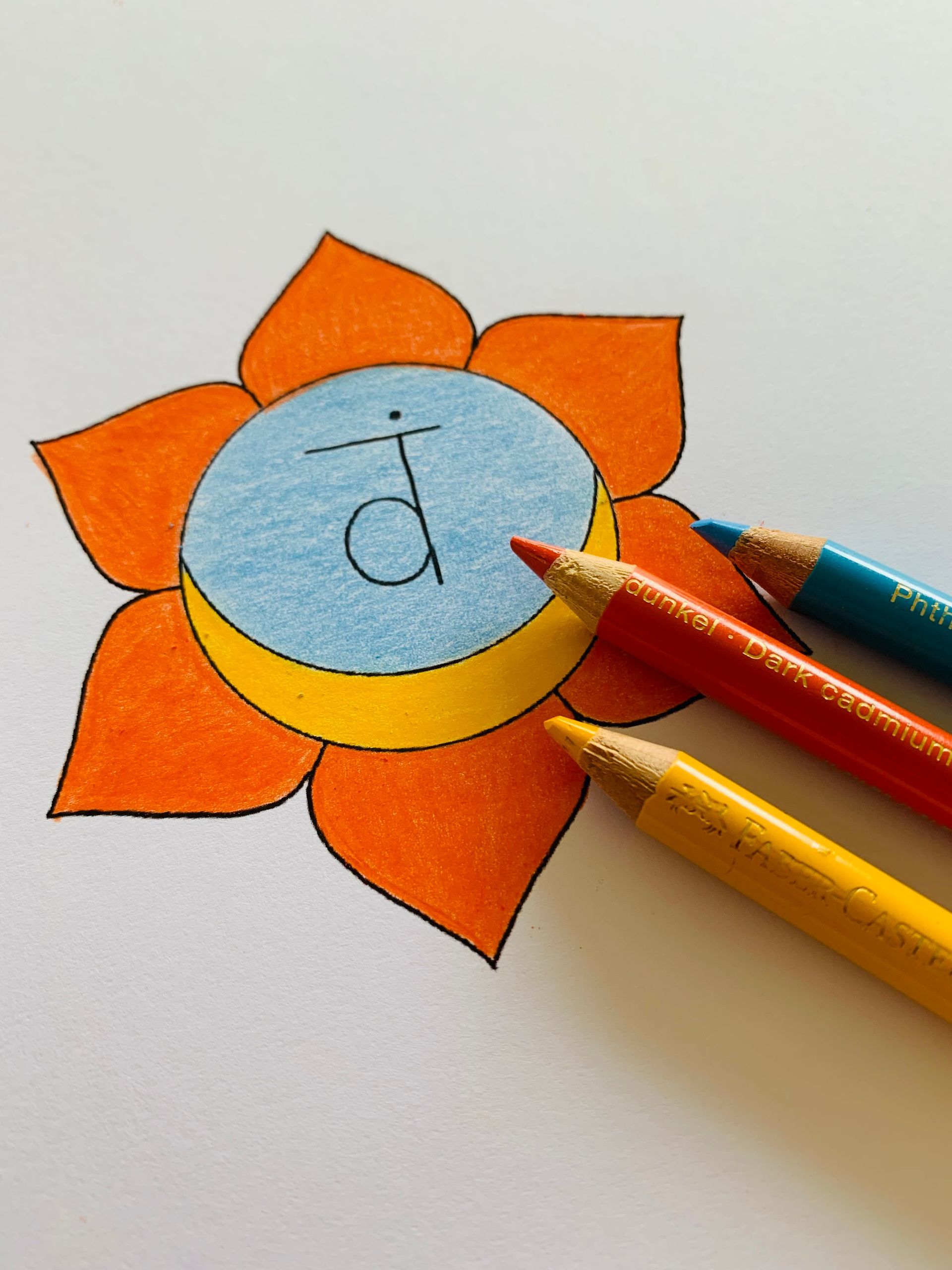 Orange chakra drawing with blue, orange, yellow pencils on white paper.