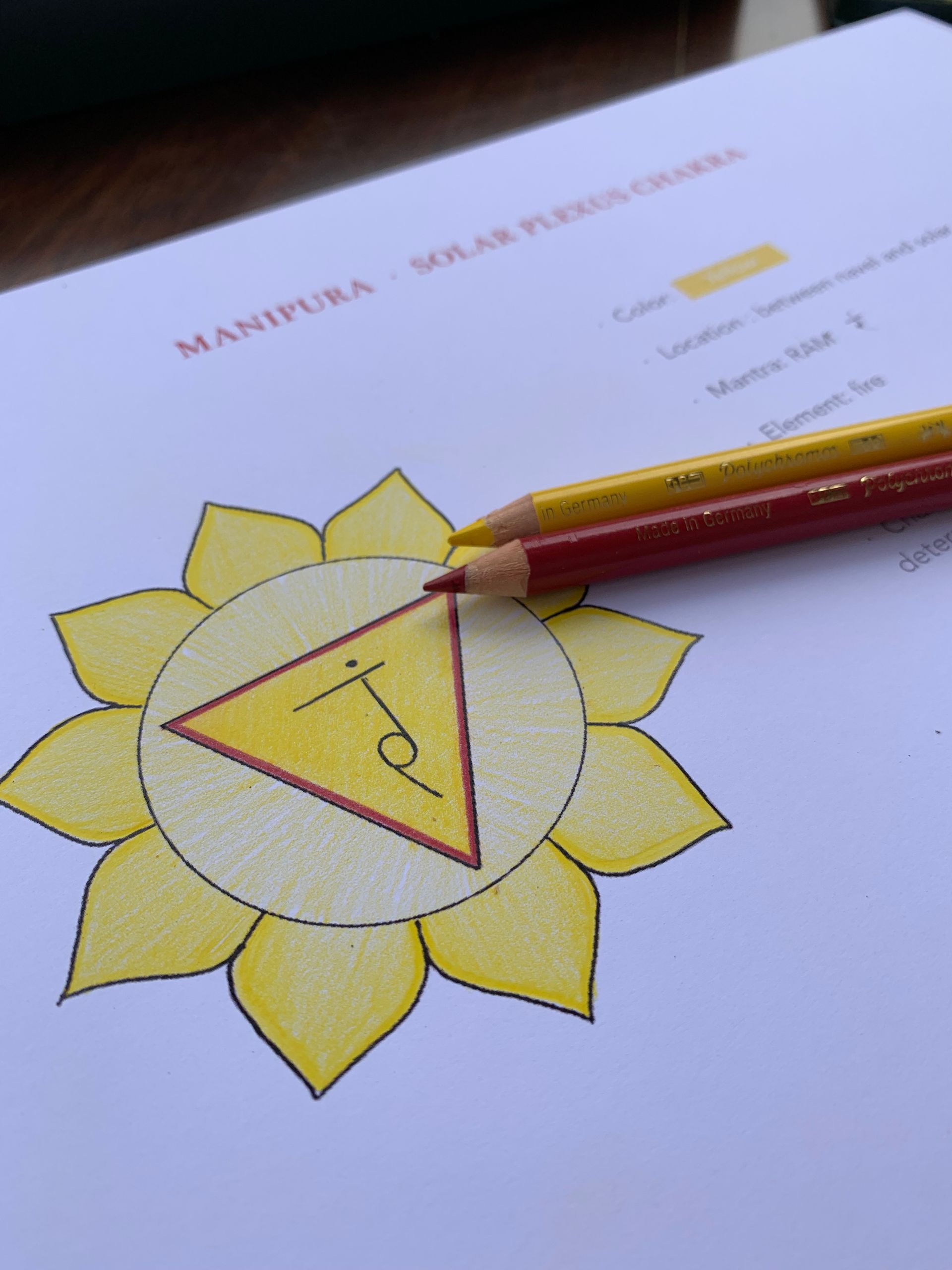 Hand-drawn solar plexus chakra with yellow flower petals, a yellow triangle, and two colored pencils.