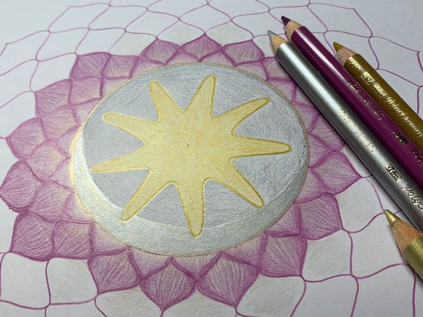 Close-up of mandala drawing in progress, featuring gold star, metallic silver, and pink, with colored pencils.