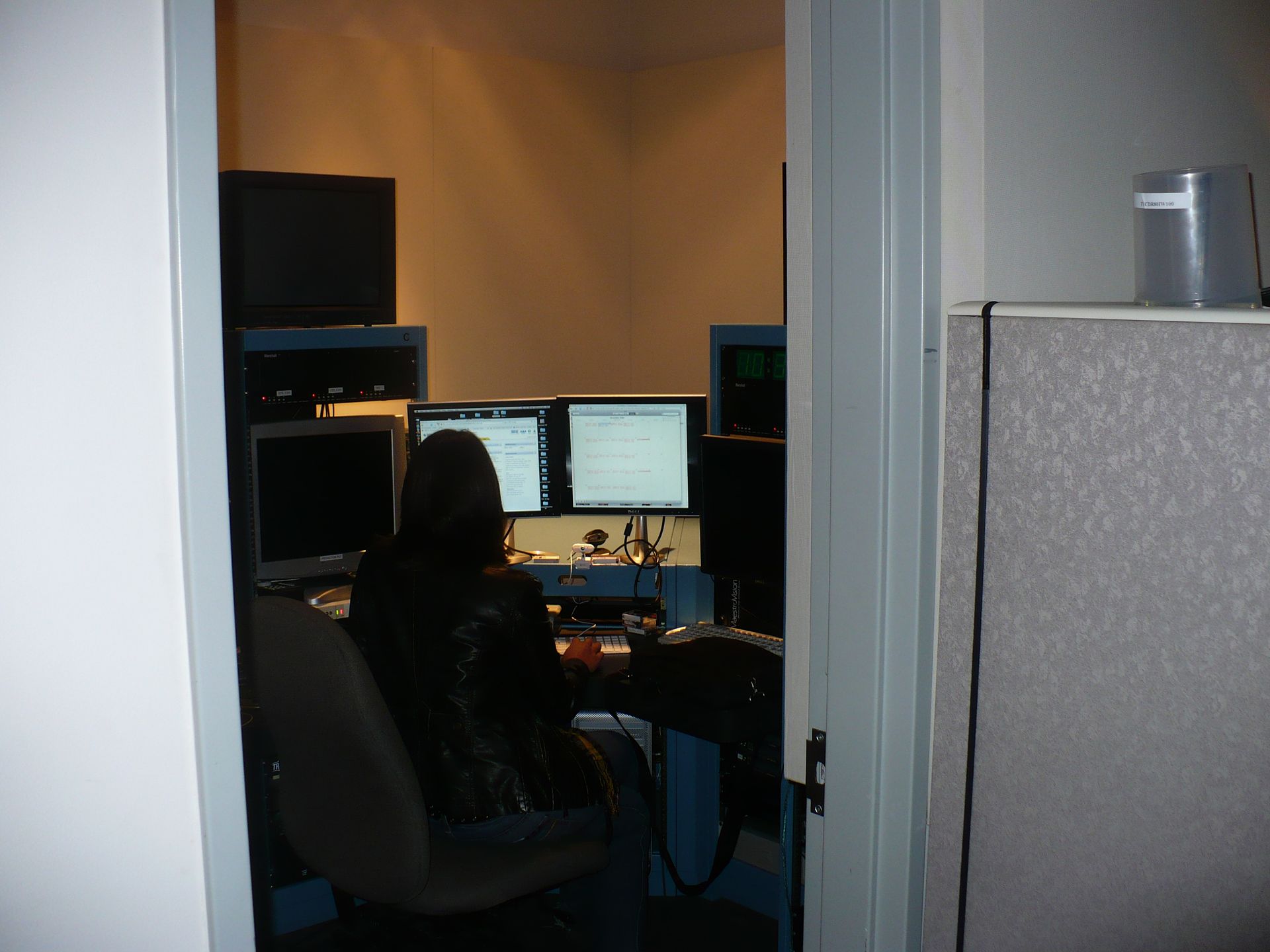A woman sits at a desk with three computer monitors