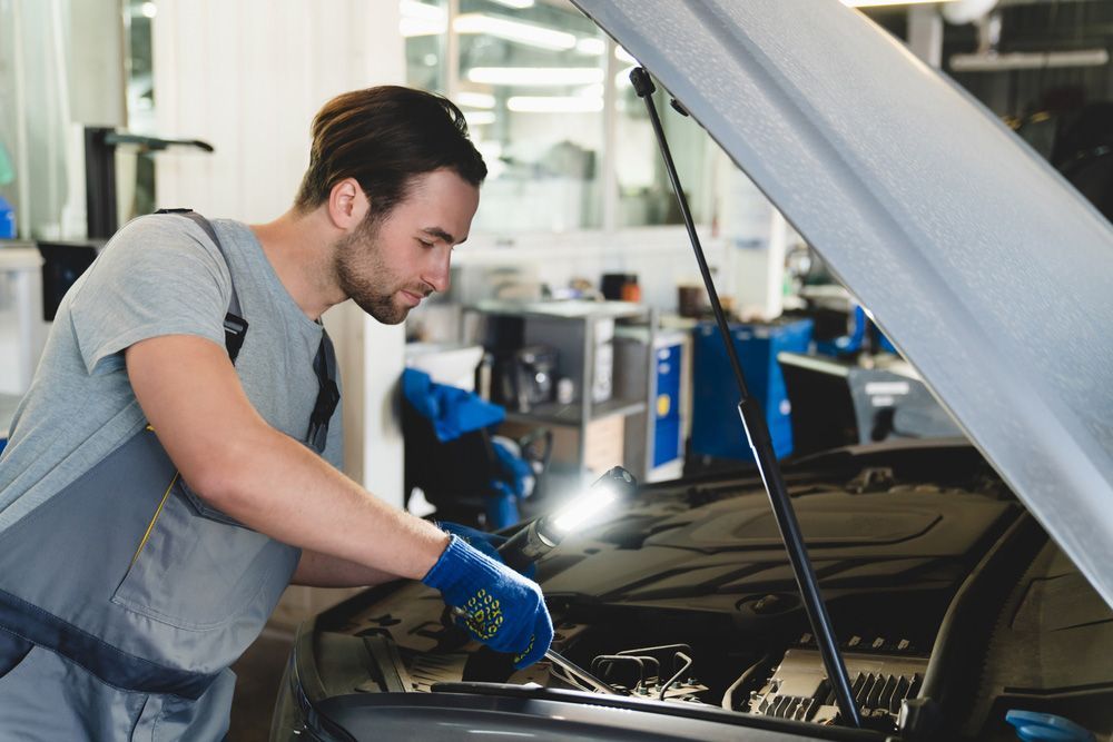 A Man Is Working On A Car In A Garage With The Hood Open — Too Ezy Auto Electrics In Townsville, QLD