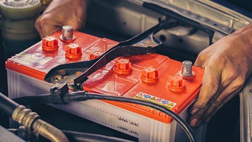 A Person Is Plugging A Red Battery Into A Car — Too Ezy Auto Electrics In Townsville, QLD