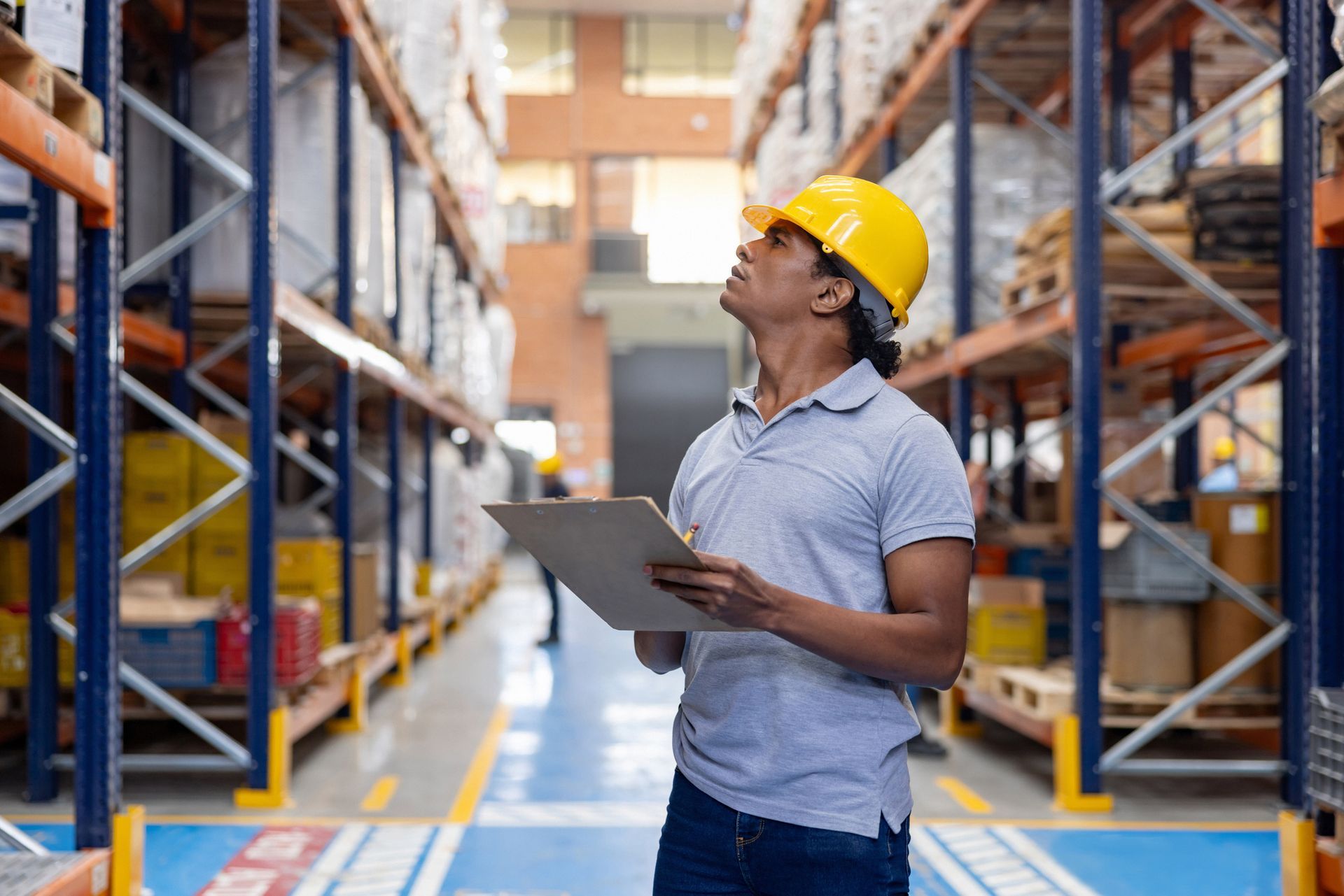 A man in a hard hat is standing in a warehouse holding a clipboard. A man in a hard hat is standing in a warehouse holding a clipboard.