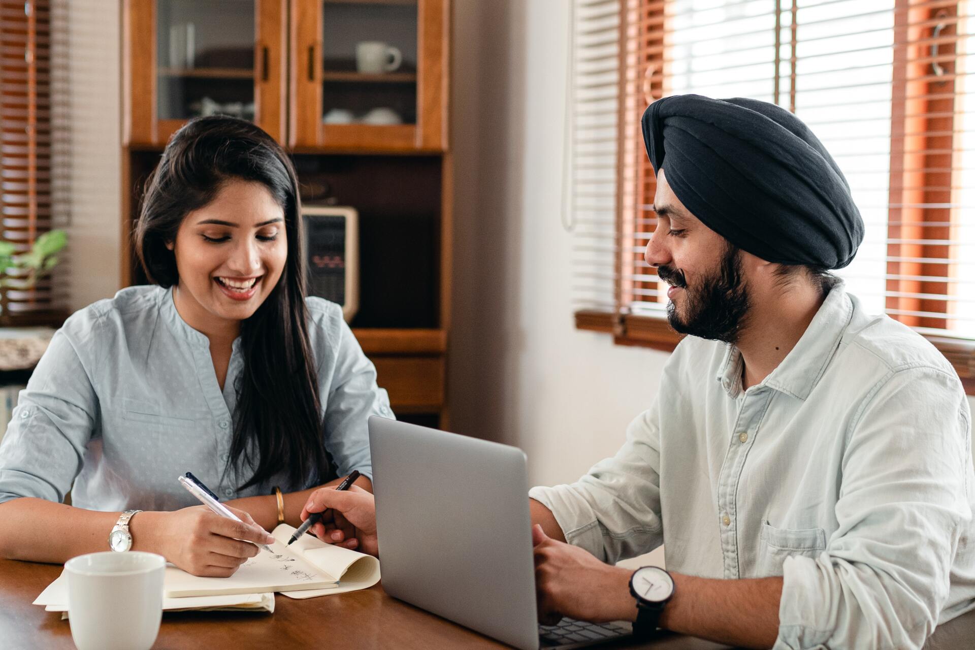 Two adults working cheerily together using a laptop and notebook