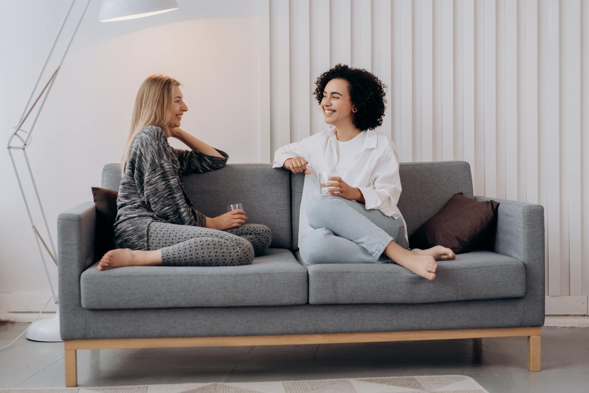 Two women smiling and talking to each other sat on a couch in a relaxed setting