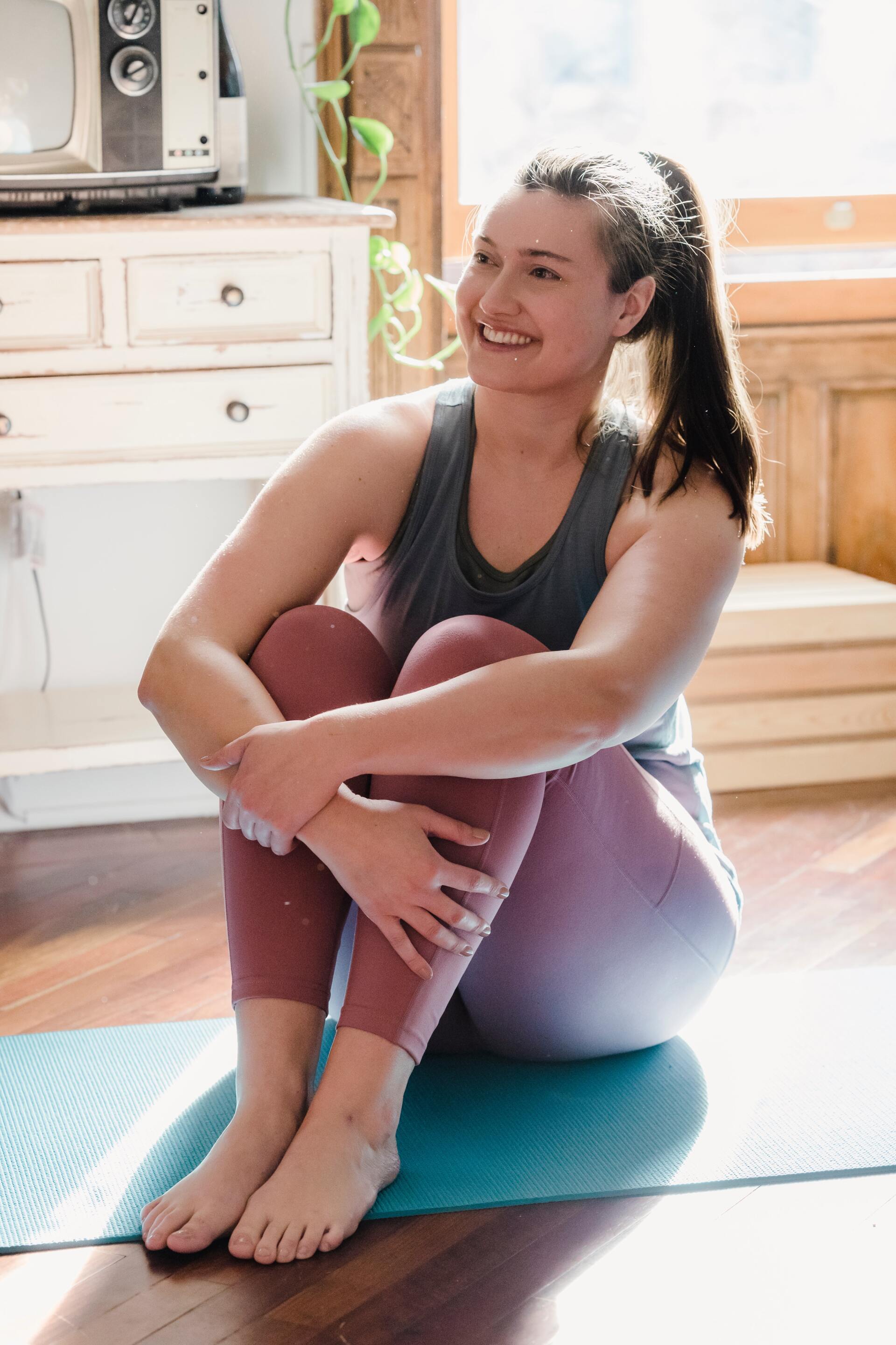 A happy young adult sat on the floor in yoga wear