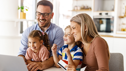 A family sitting at a table looking at a laptop computer