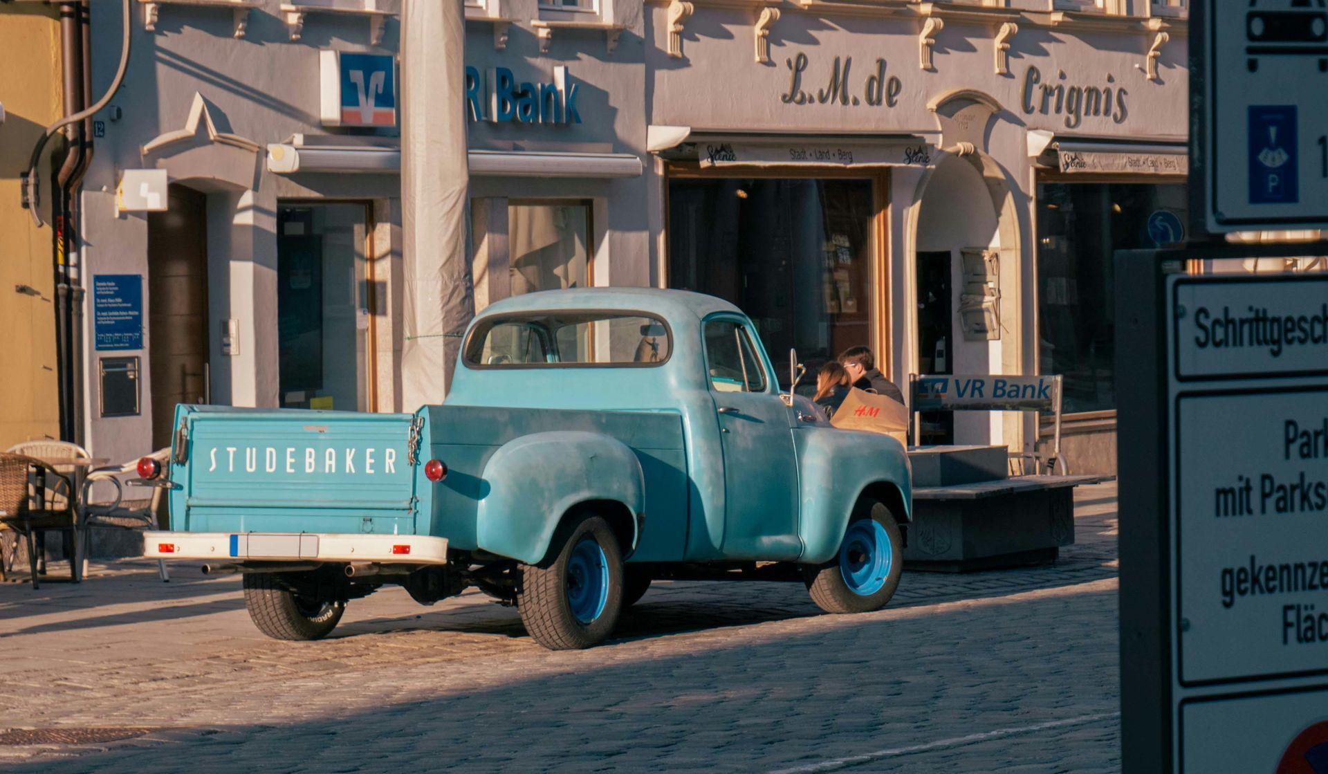 A blue Studebaker truck is parked in front of a building.