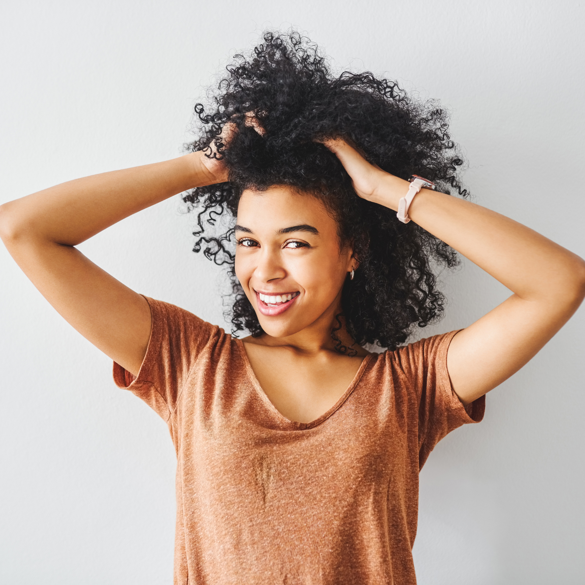 A woman with curly hair is smiling with her hands in her hair.