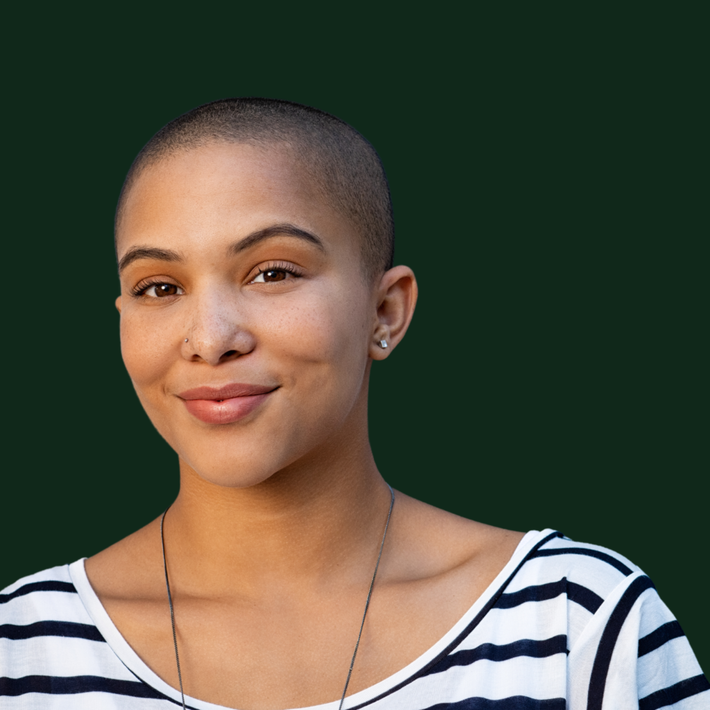 A woman with a shaved head is wearing a striped shirt and smiling.