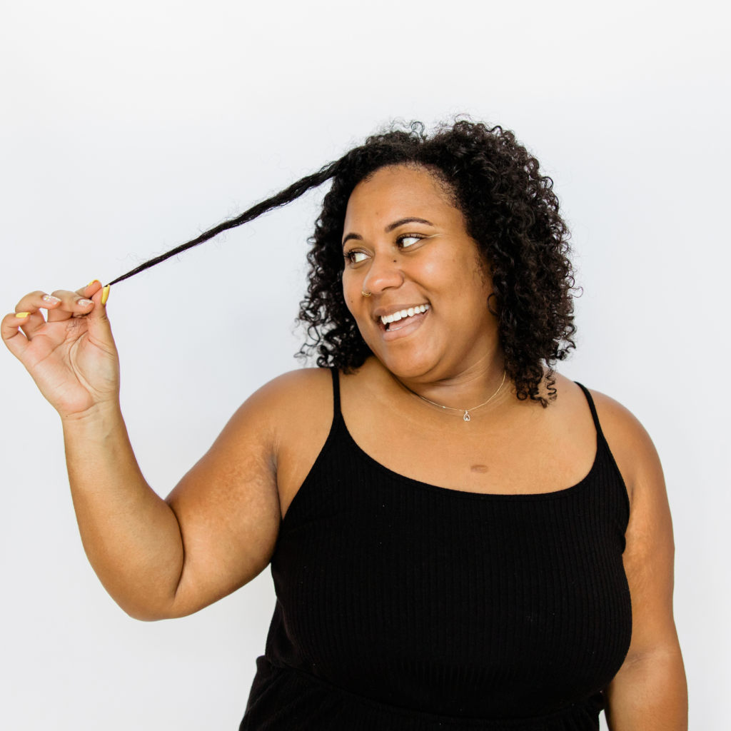 A woman in a black tank top is smiling and holding her hair.