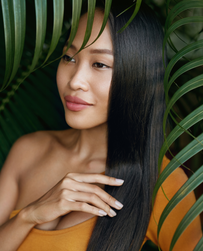 A woman with long black hair is standing in front of a palm tree.