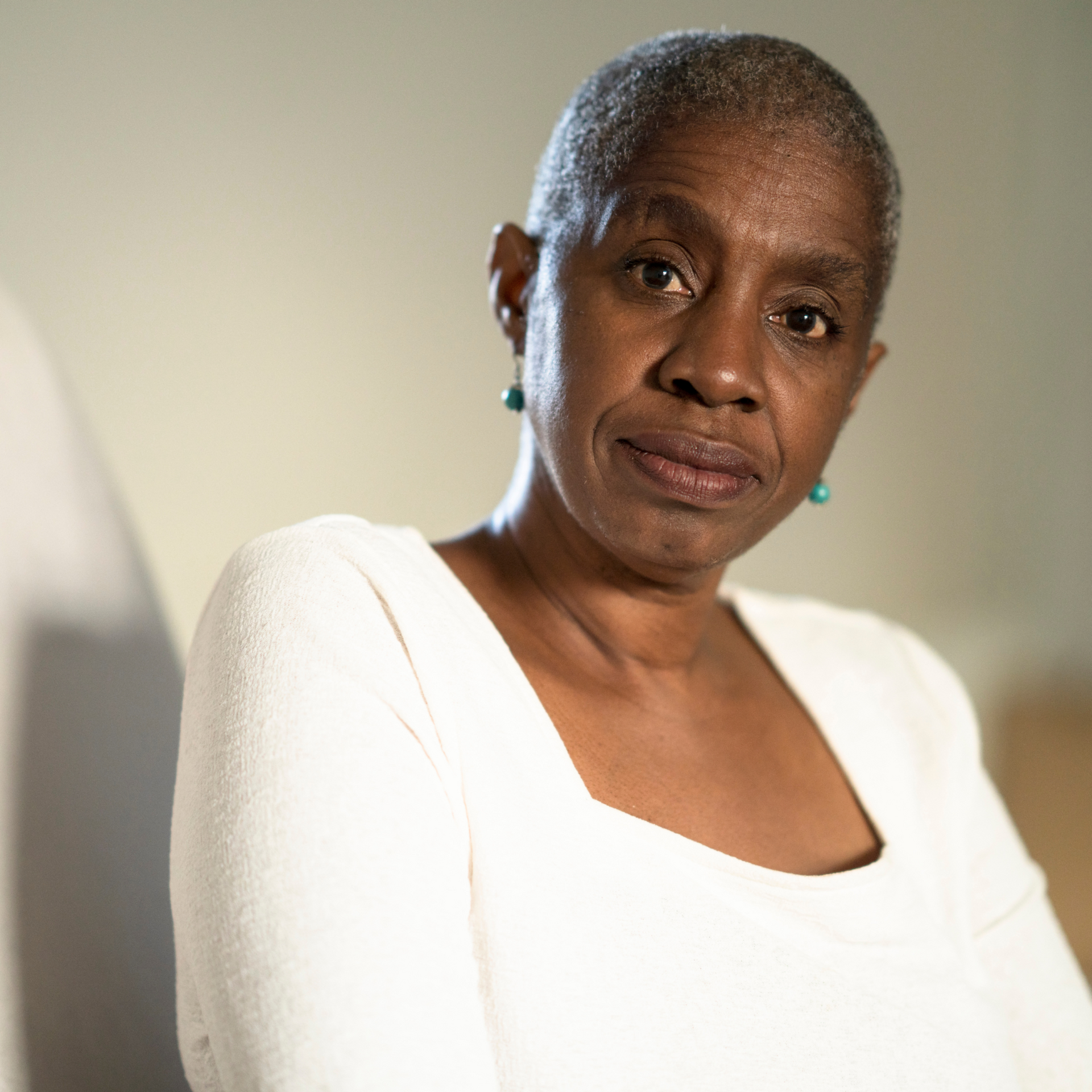 A woman wearing a white sweater and earrings is looking at the camera.