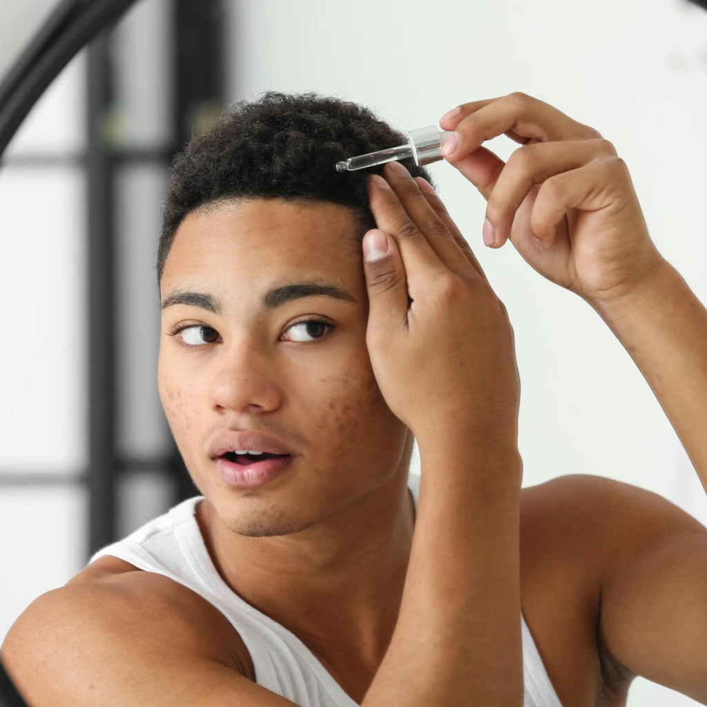 A man is applying a serum to his hair in front of a mirror