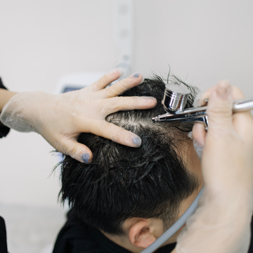 A man is getting an airbrush treatment on his head.