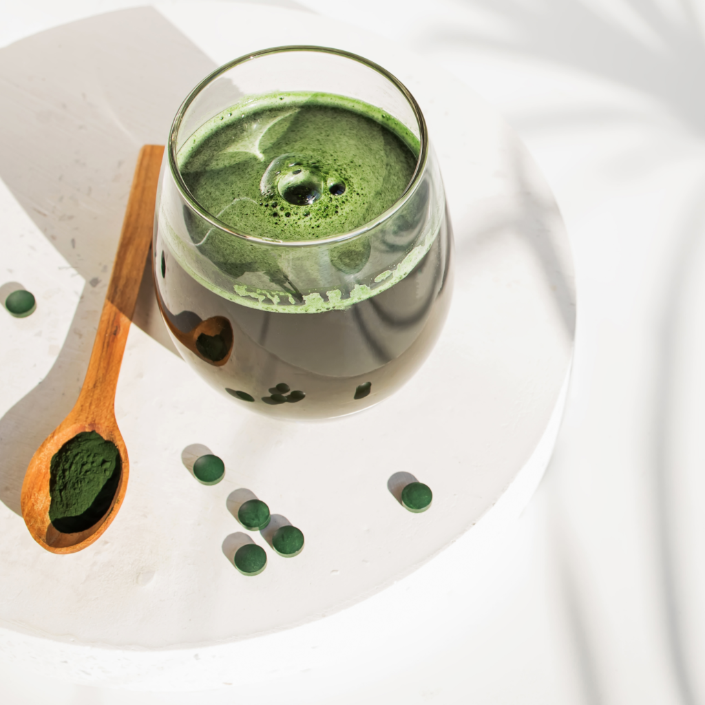 A glass of green liquid next to a wooden spoon