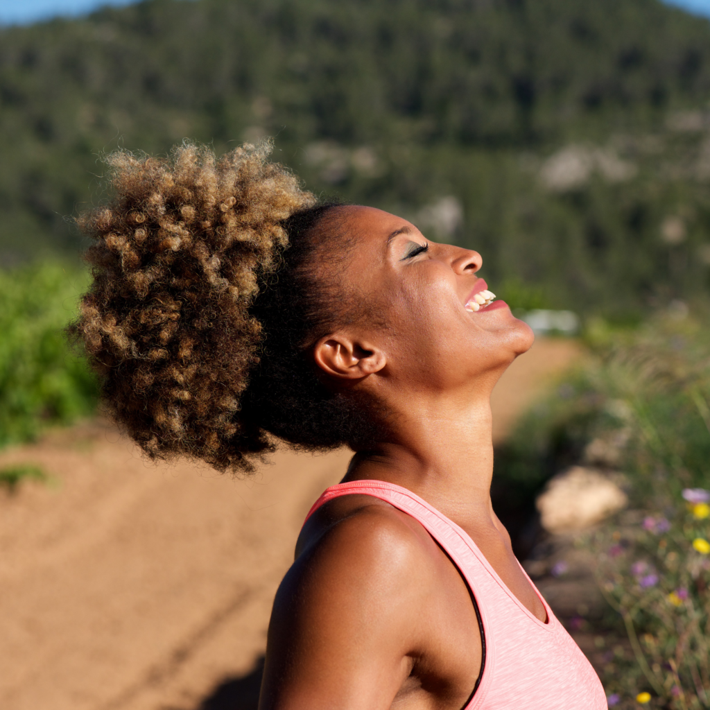 A woman with curly hair is smiling and looking up at the sky.