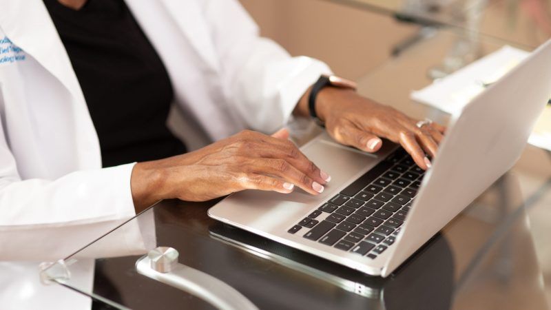 A woman in a lab coat is typing on a laptop computer.